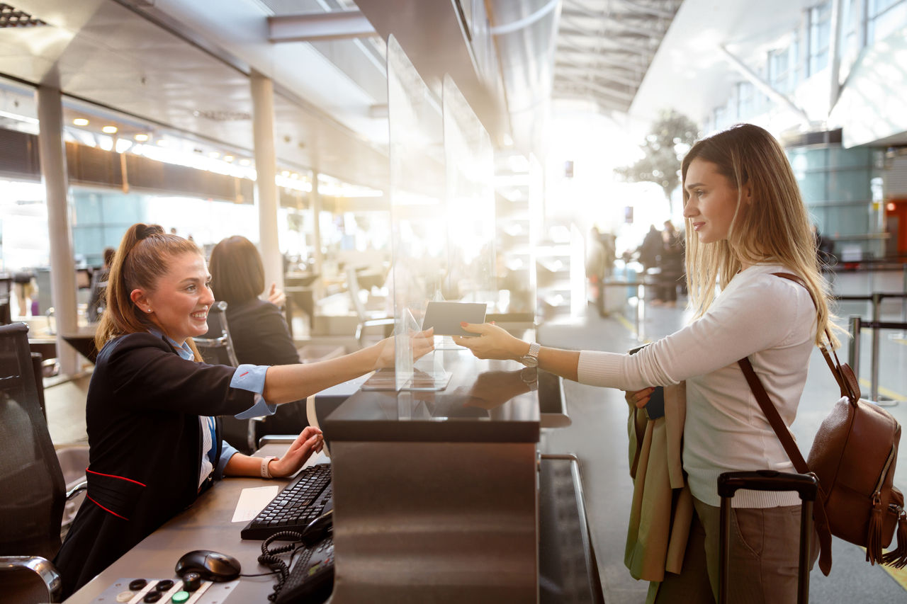Side view of smiling woman giving her passport to an airport staff member