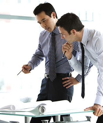 dva zaměstnanci stojící a studující dokumenty na stole